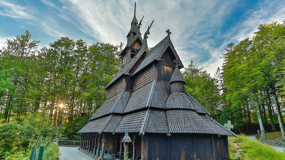 Eine traditionelle Holzkirche mit steilem Dach und einem Kreuz, umgeben von üppigem Grün.