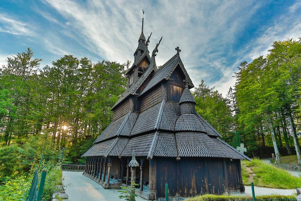 A traditional wooden church with a steeply pitched roof and a cross on top, surrounded by lush greenery.