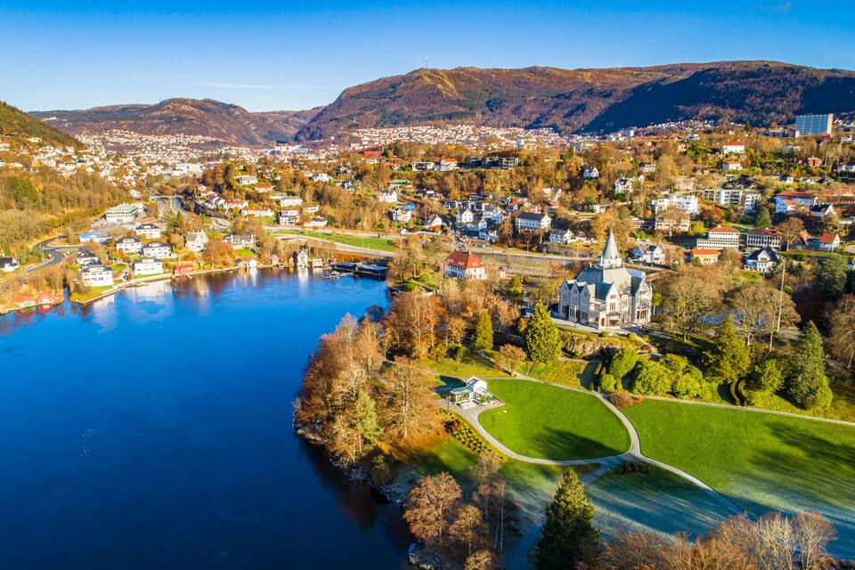 A town by a lake with a prominent church and mountains in the background.