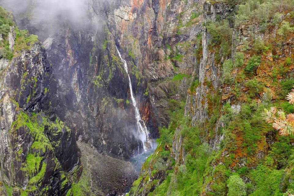 A waterfall cascading down a rocky cliff surrounded by lush greenery.