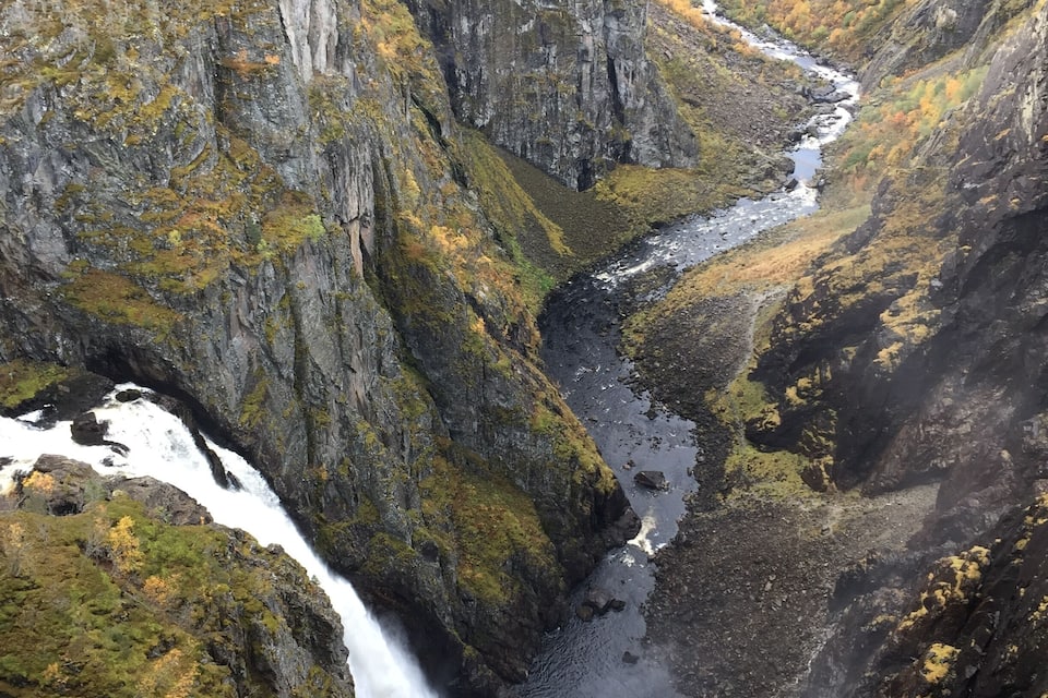 A canyon with a waterfall, rocky cliffs, and autumn foliage.