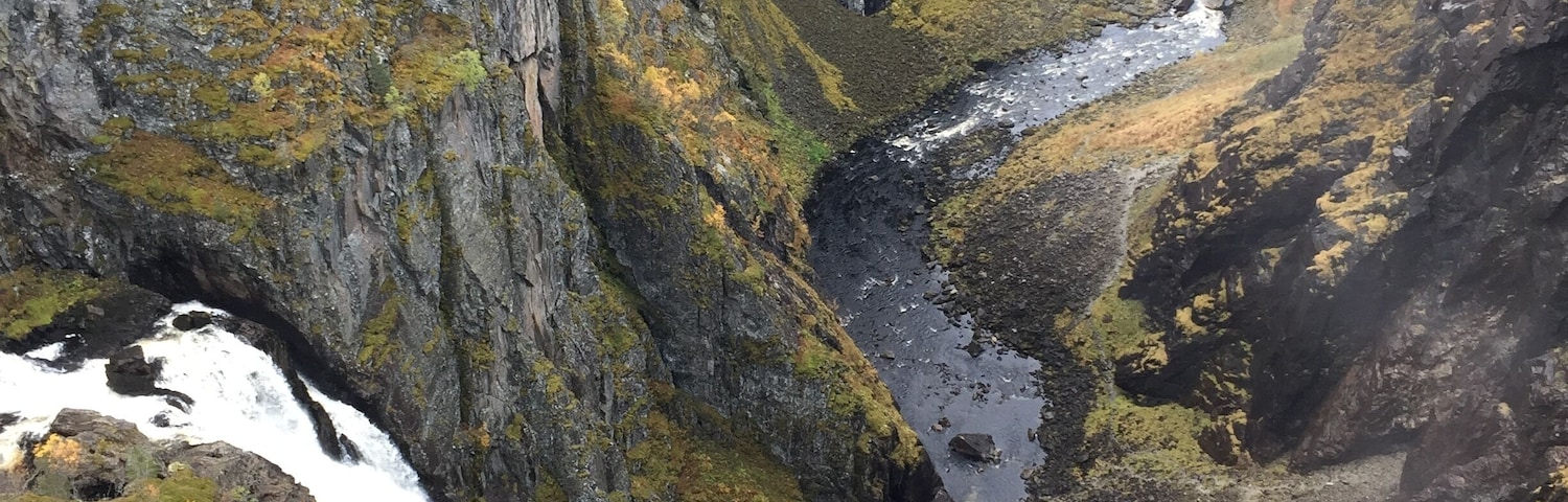 A canyon with a waterfall, rocky cliffs, and autumn foliage.