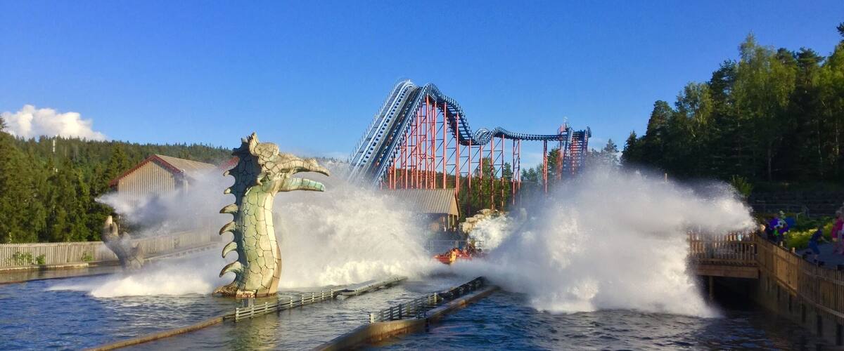 A water park with a dragon statue and a roller coaster in the background.