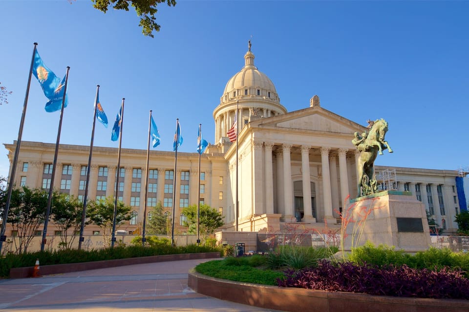 A government building with a large dome and columns, surrounded by flags and a statue.