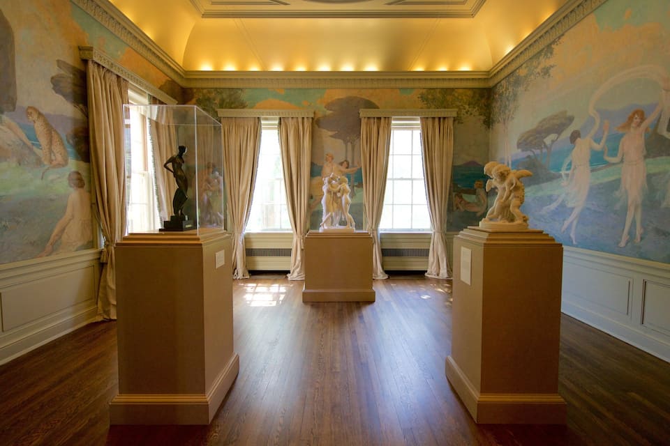 Uma sala imponente com afrescos clássicos, pisos de madeira e esculturas clássicas em pedestais.