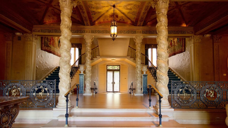 A grand hall with ornate columns, a staircase, and a chandelier.