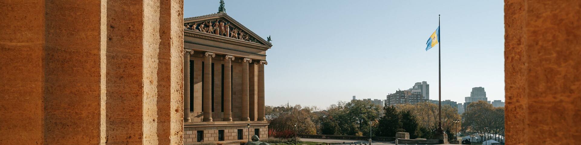 A large classical building with columns, a flag, and a statue in a square.