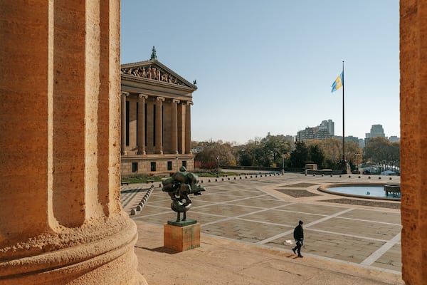 Un grand bâtiment de style classique, orné de colonnes, surmonté d’un drapeau et abritant une statue, le tout situé sur une place.