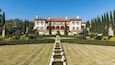 Un vaste domaine agrémenté d’un jardin à la disposition symétrique, d’une fontaine centrale et d’un ciel d’un bleu éclatant.