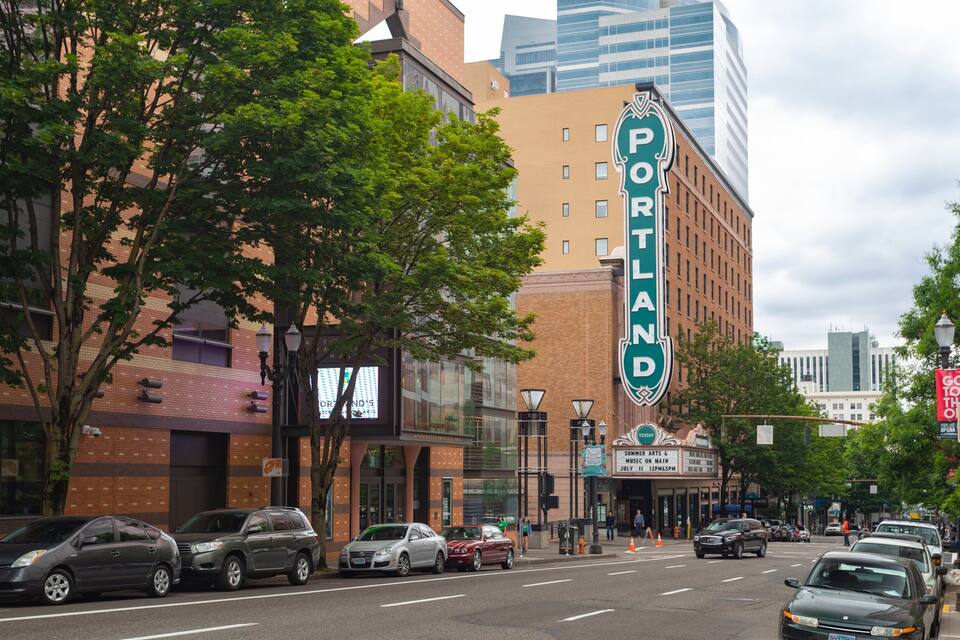 A street with cars, trees, and a Portland theater sign.