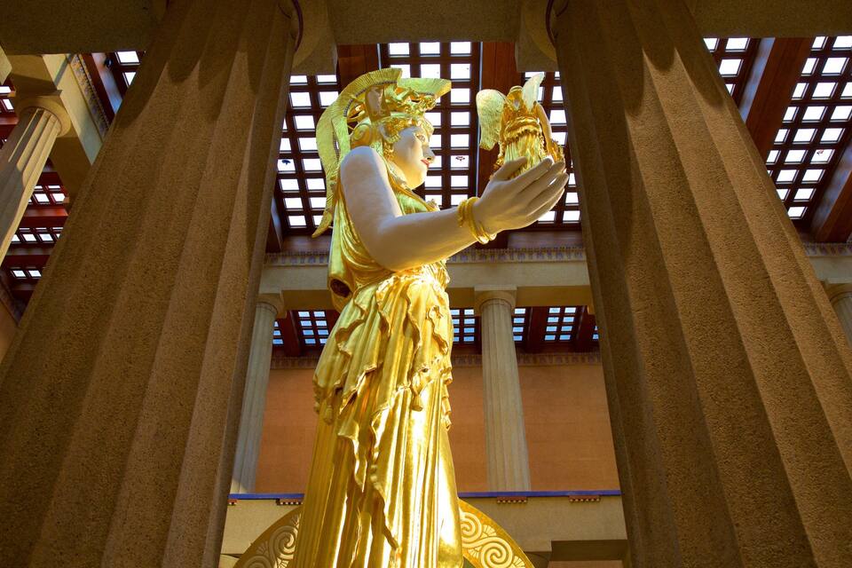 Una statua dorata in un contesto architettonico con colonne e finestre decorate.