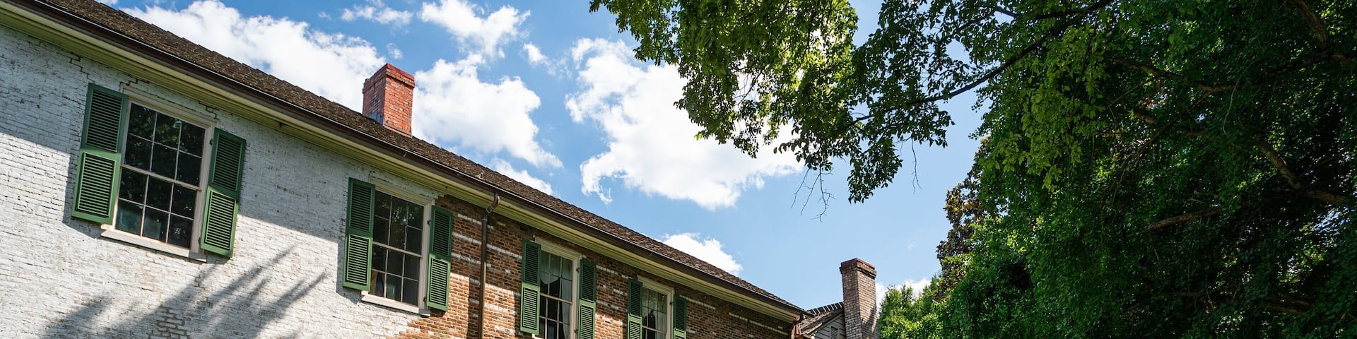 A historic brick building with green shutters and a well-maintained lawn.