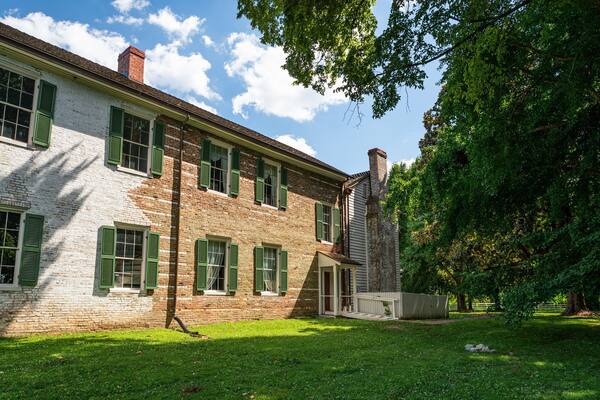 A historic brick building with green shutters and a well-maintained lawn.
