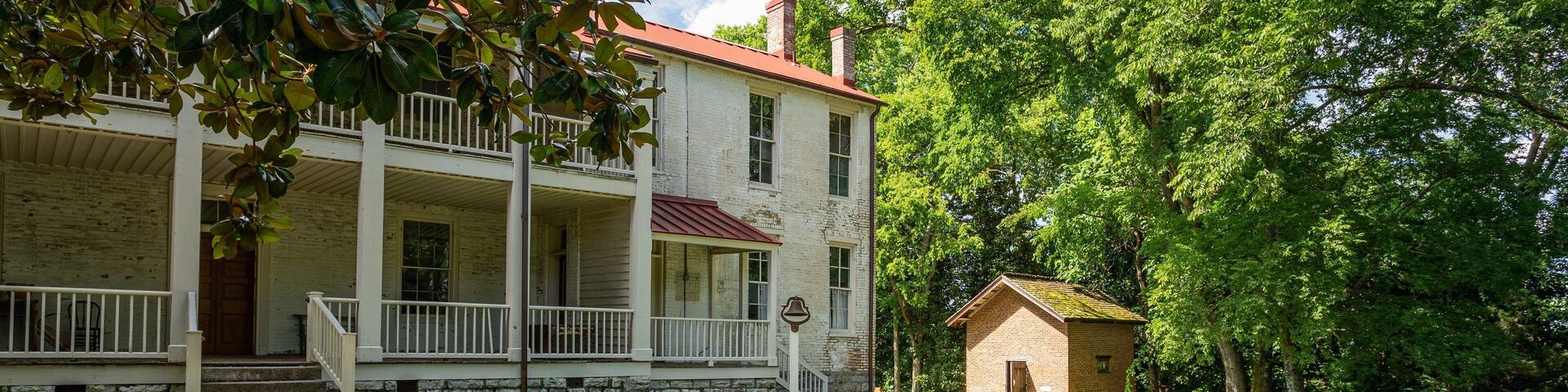 A historic white building with a red roof, a covered porch, and a small brick structure nearby.