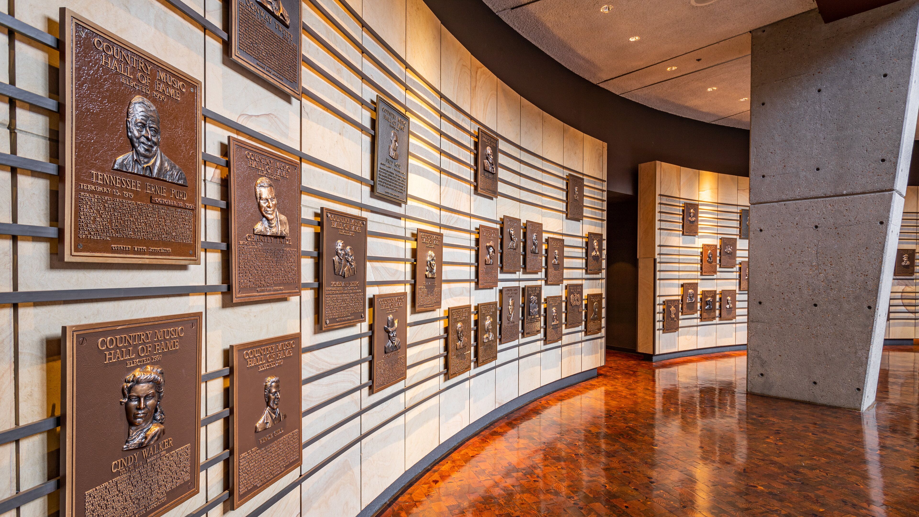 Paredão de placas de bronze com bustos e texto, provavelmente em um museu ou salão memorial.