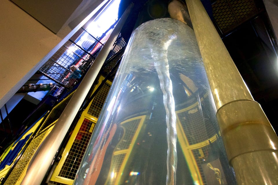 A large cylindrical structure with a reflective surface, surrounded by industrial elements and metal railings.