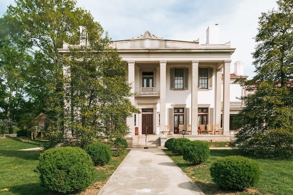 A large, stately building with columns and a balcony, surrounded by well-maintained lawns and trees.