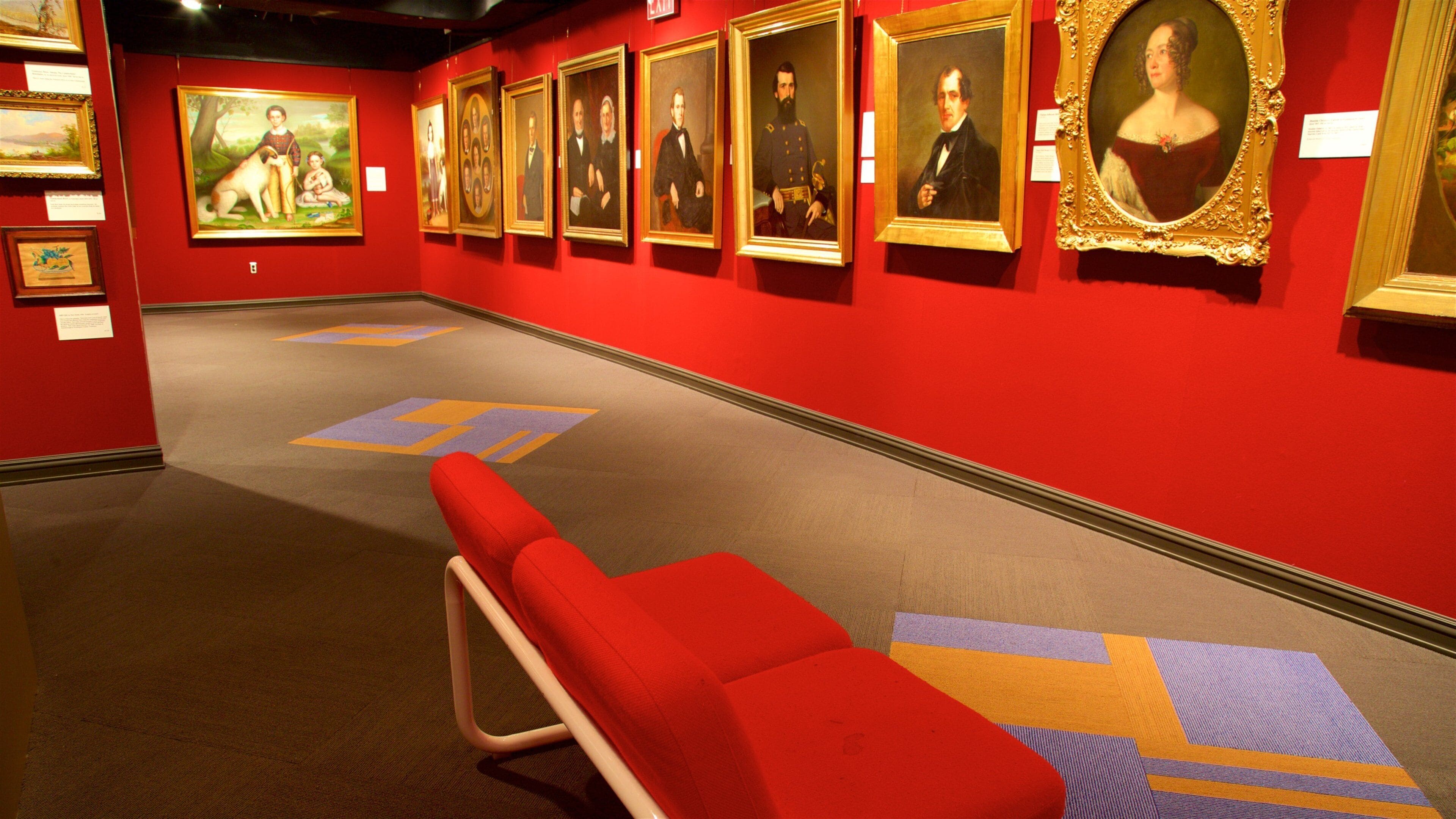 An art gallery with red walls and a red bench.