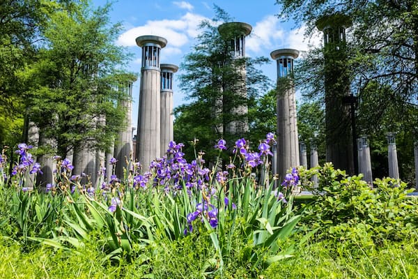 A garden with tall stone columns, purple flowers, and lush green trees.