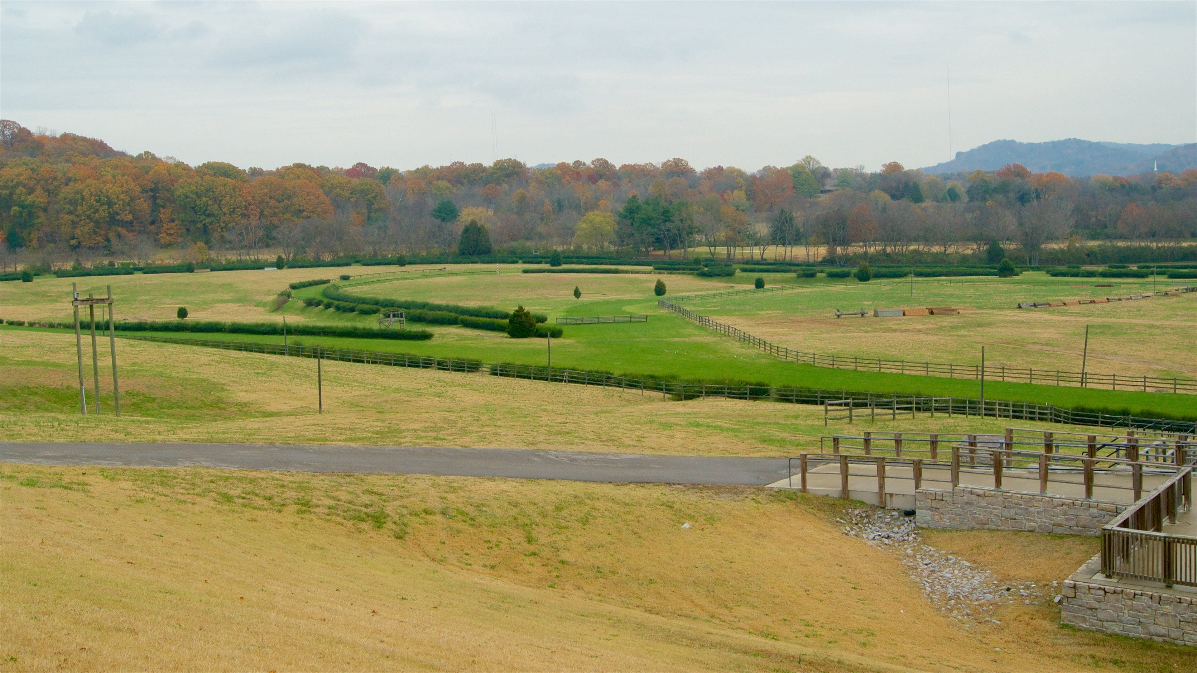 A rural landscape with rolling hills, a fenced field, and a stone bridge.