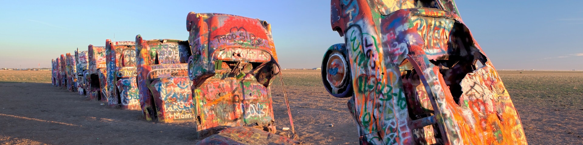 A row of colorful, graffiti-covered vehicles parked in a desert.