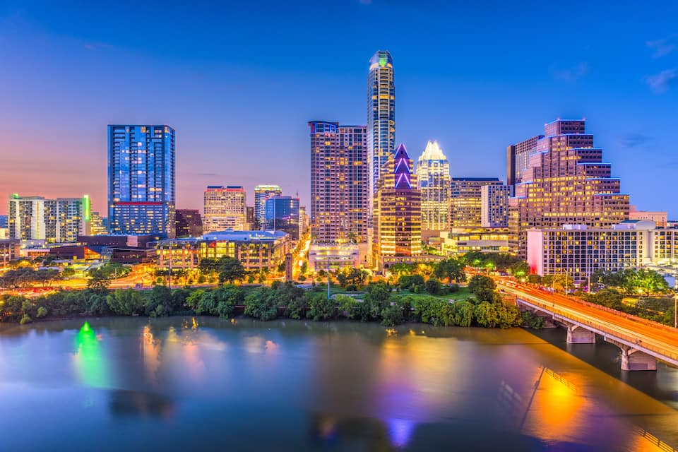 A city skyline with illuminated buildings, a river, and a bridge.