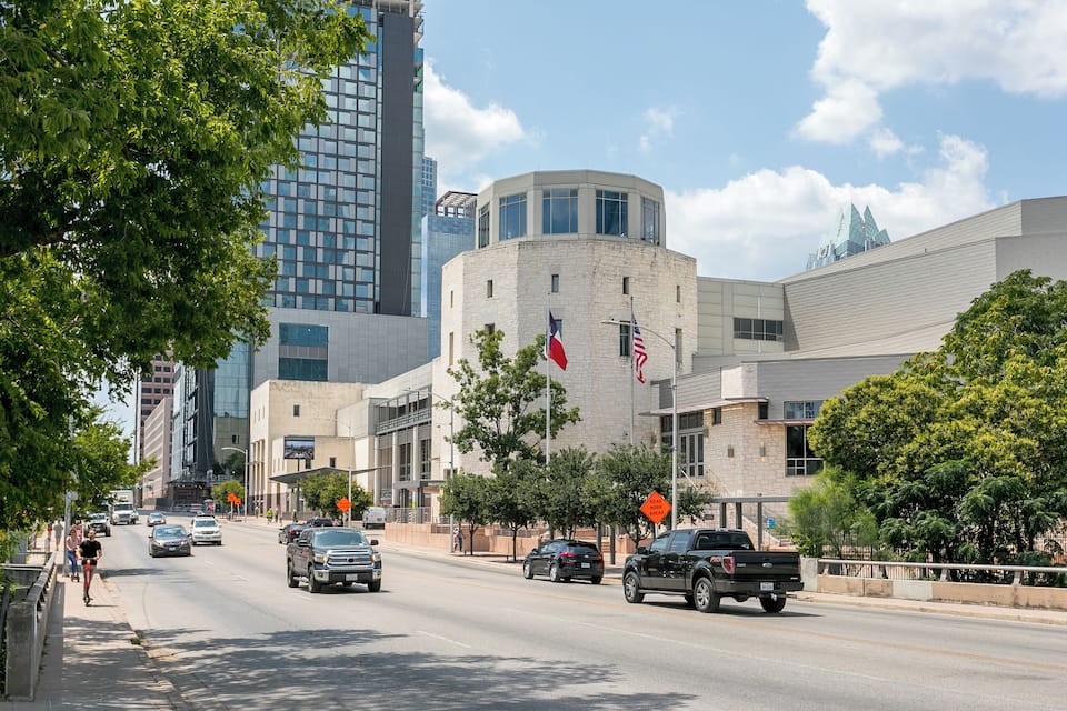 A city street with modern buildings, a large flag, and a clear blue sky.