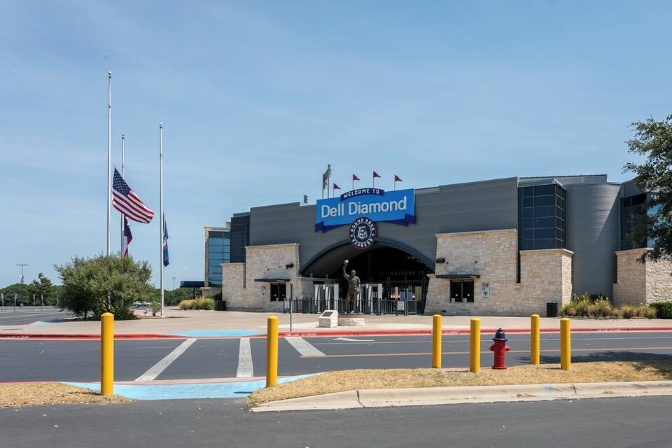 A building with a 'Welcome to Dell Diamond' sign, American flags, and a statue.
