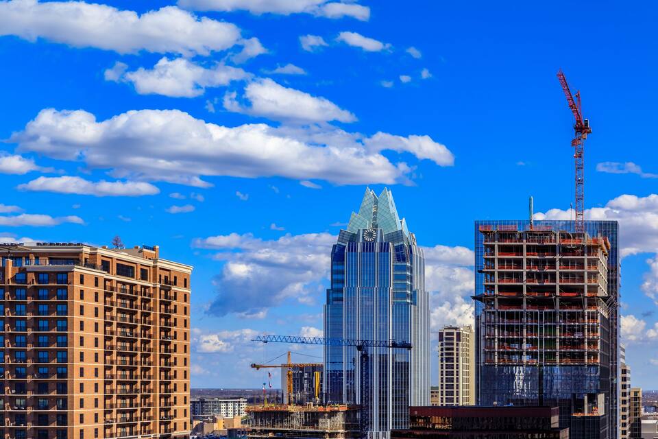 A cityscape with a tall building under construction, a crane, and a clear blue sky with clouds.