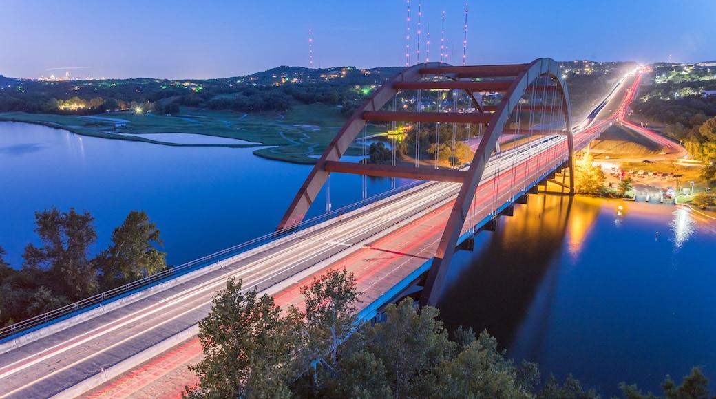 View of Pennybacker Bridge or 360 Bridge from limestone cliffs. A landmark in Austin, Texas, USA at blue hour with colorful car light trail in traffic. Top of Town Lake and Hill Country landscape.