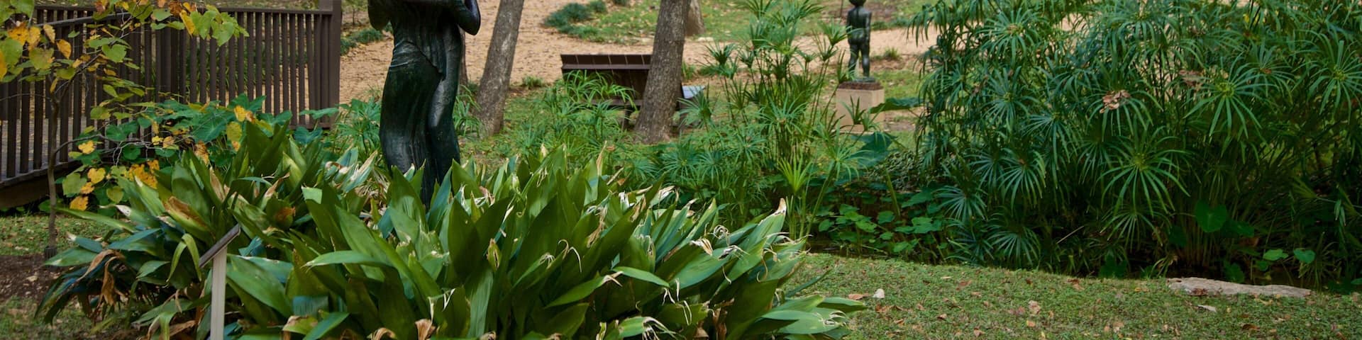 A park with statues, lush greenery, and people walking.