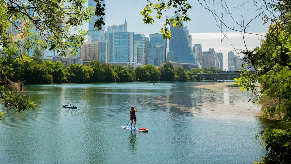 A river with paddleboarders, a city skyline in the background, and a bridge.