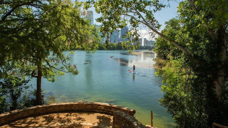 A calm lake with paddle boats, surrounded by trees and a stone bridge.