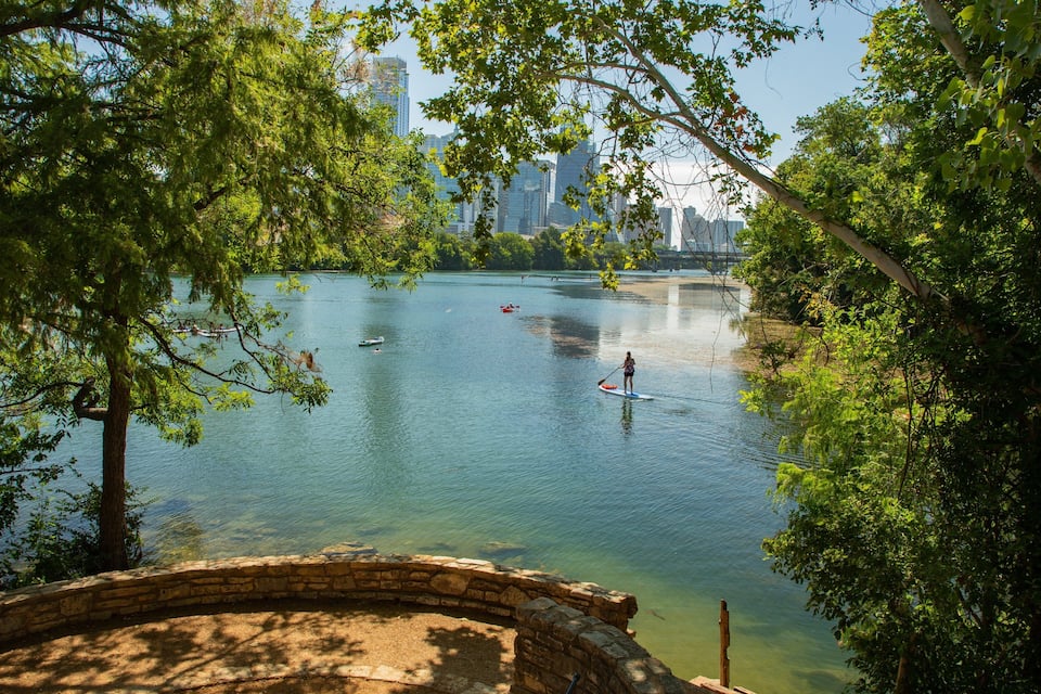 Un lago tranquilo con botes de remo, rodeado de árboles y un puente de piedra.