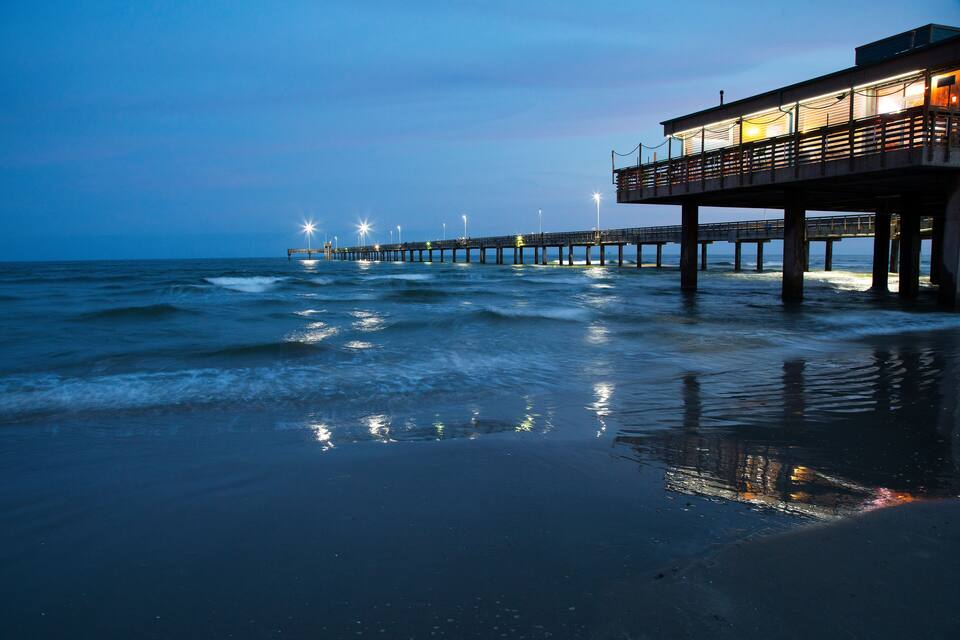 Un muelle que se adentra en el océano al anochecer, con luces a lo largo de su extensión.