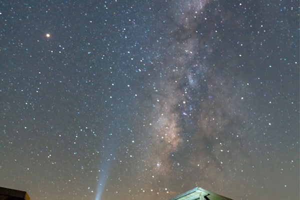 A night sky with stars and the Milky Way visible above a beach with a gazebo.