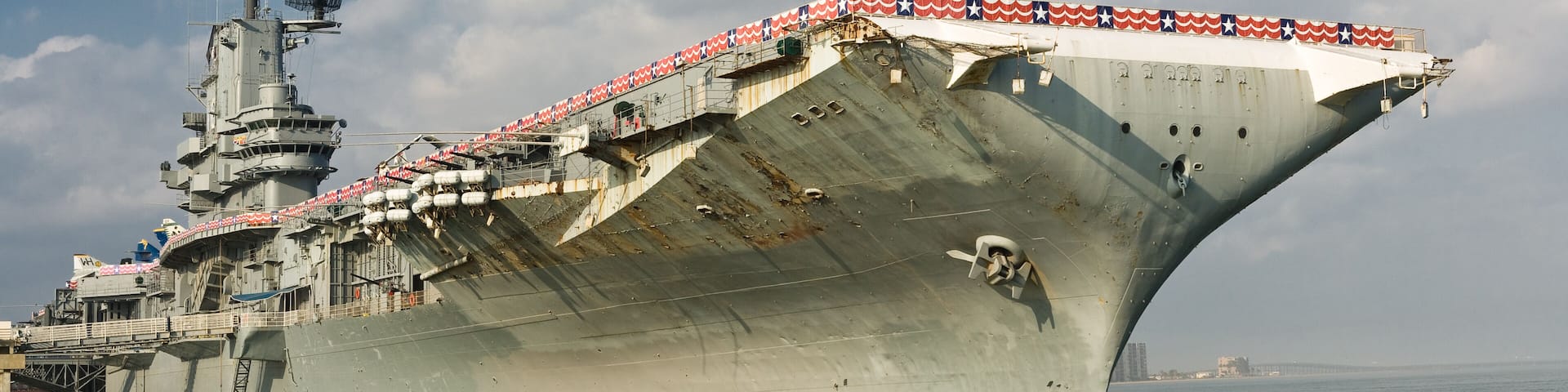 A large naval ship docked at a port with a clear sky and calm sea.