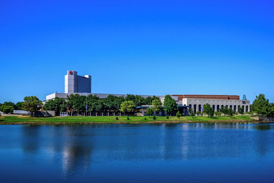 Un grande edificio con una torre e finestre ad arco, circondato da alberi e un lago.