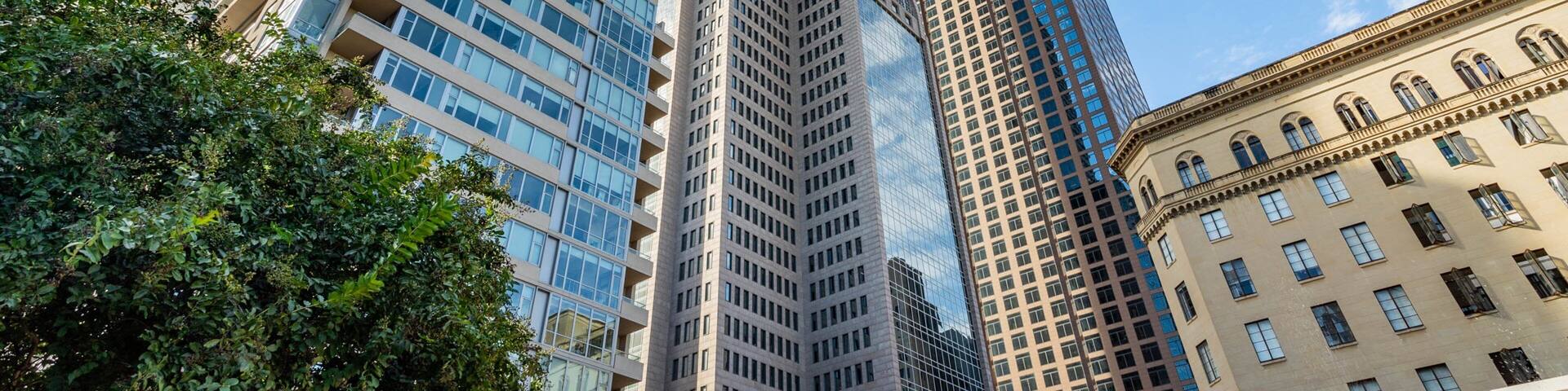 A cityscape with modern skyscrapers, including a tall glass building and a historic building with arched windows.