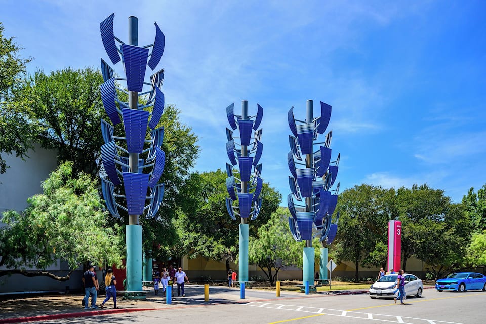 A street with three blue, abstract sculptures and a red sign with the number 3.