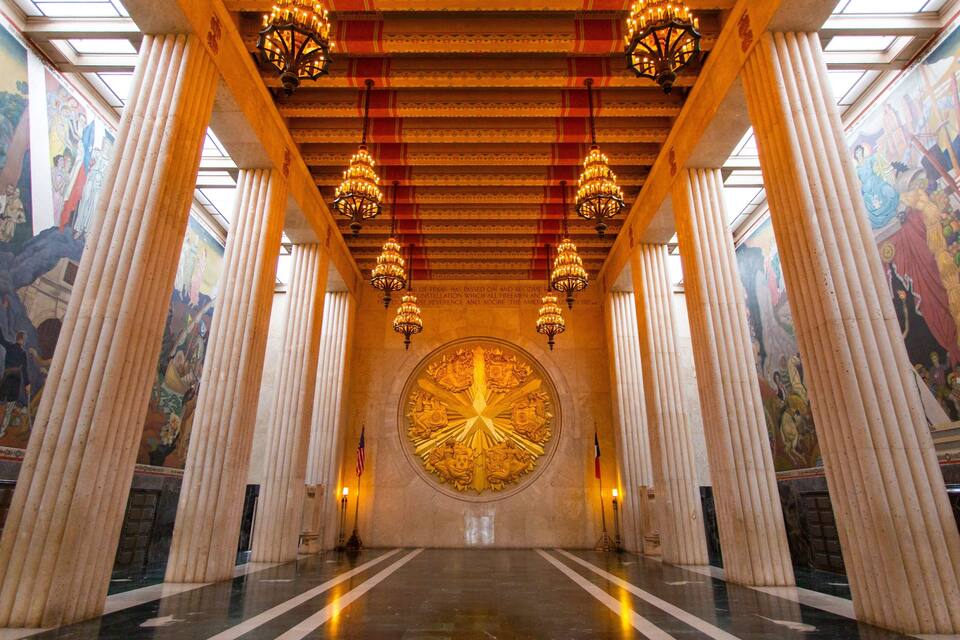 A grand hall with tall columns, ornate chandeliers, and detailed murals on the walls.