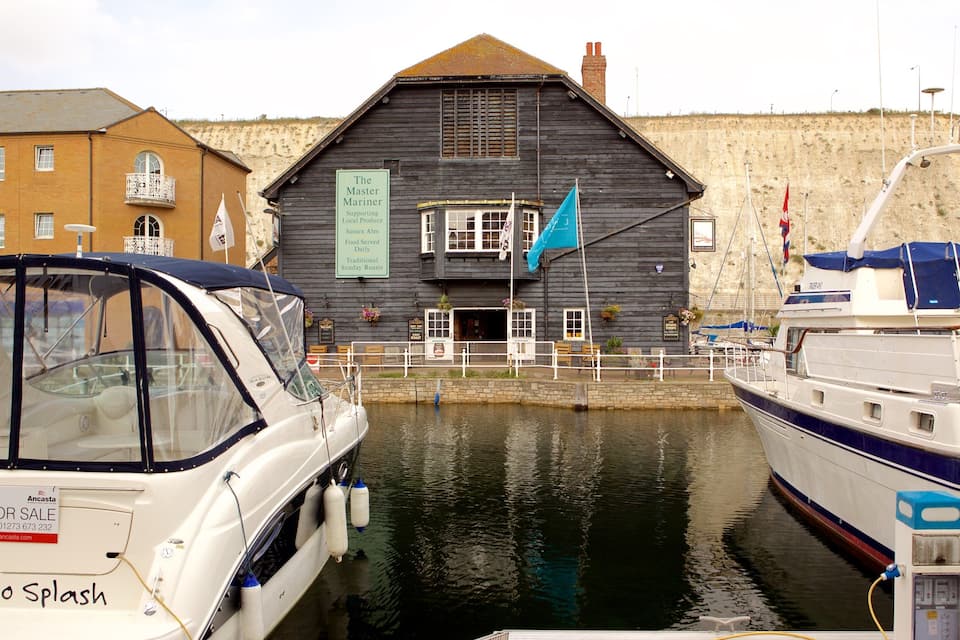A harbor with boats docked, a wooden building with flags, and a signboard.