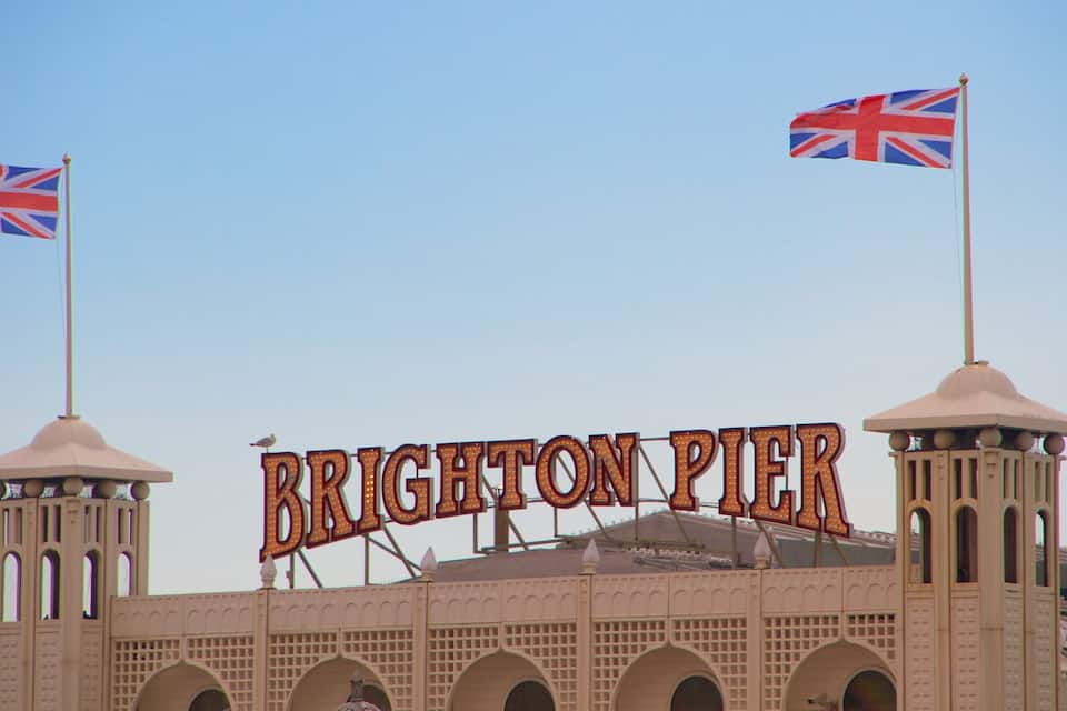 La entrada del muelle Brighton con dos banderas y señalización iluminada.
