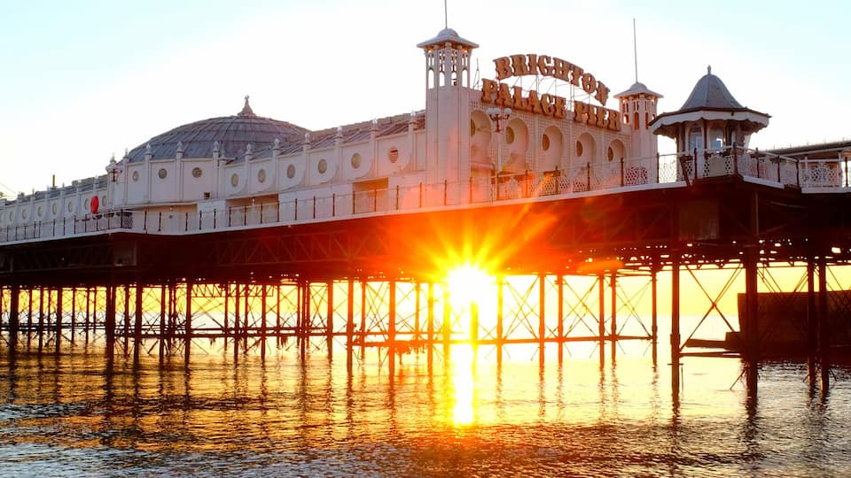 Brighton Palace Pier glowing yellow with the sun setting underneath it reflecting on a calm sea