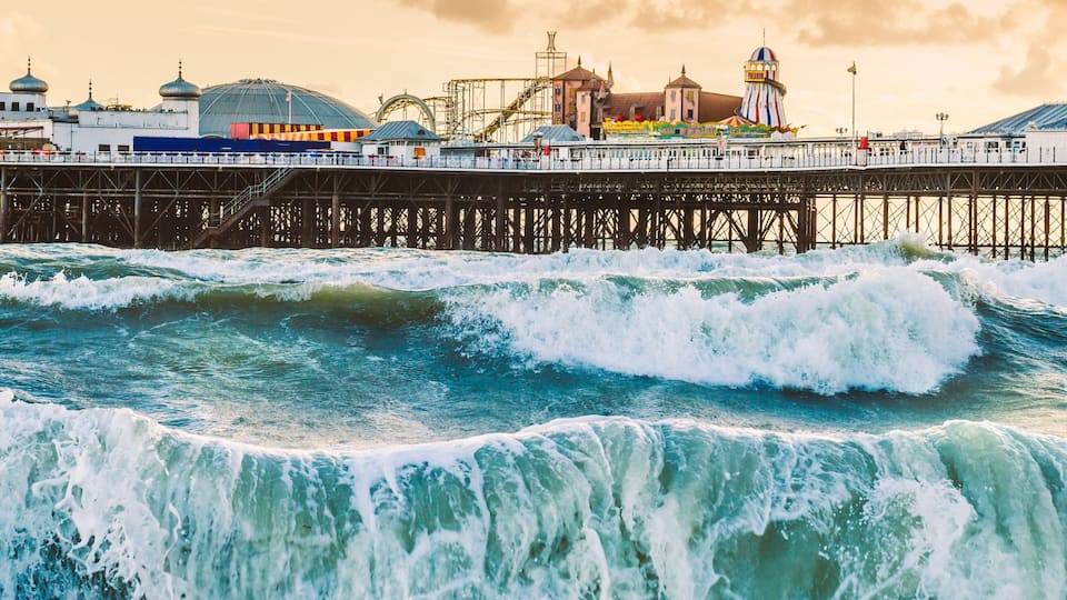 Brighton Pier, Brighton, Sussex, Britain on a storm evening at dusk as the sun is setting. There are high waves and surf on the beach