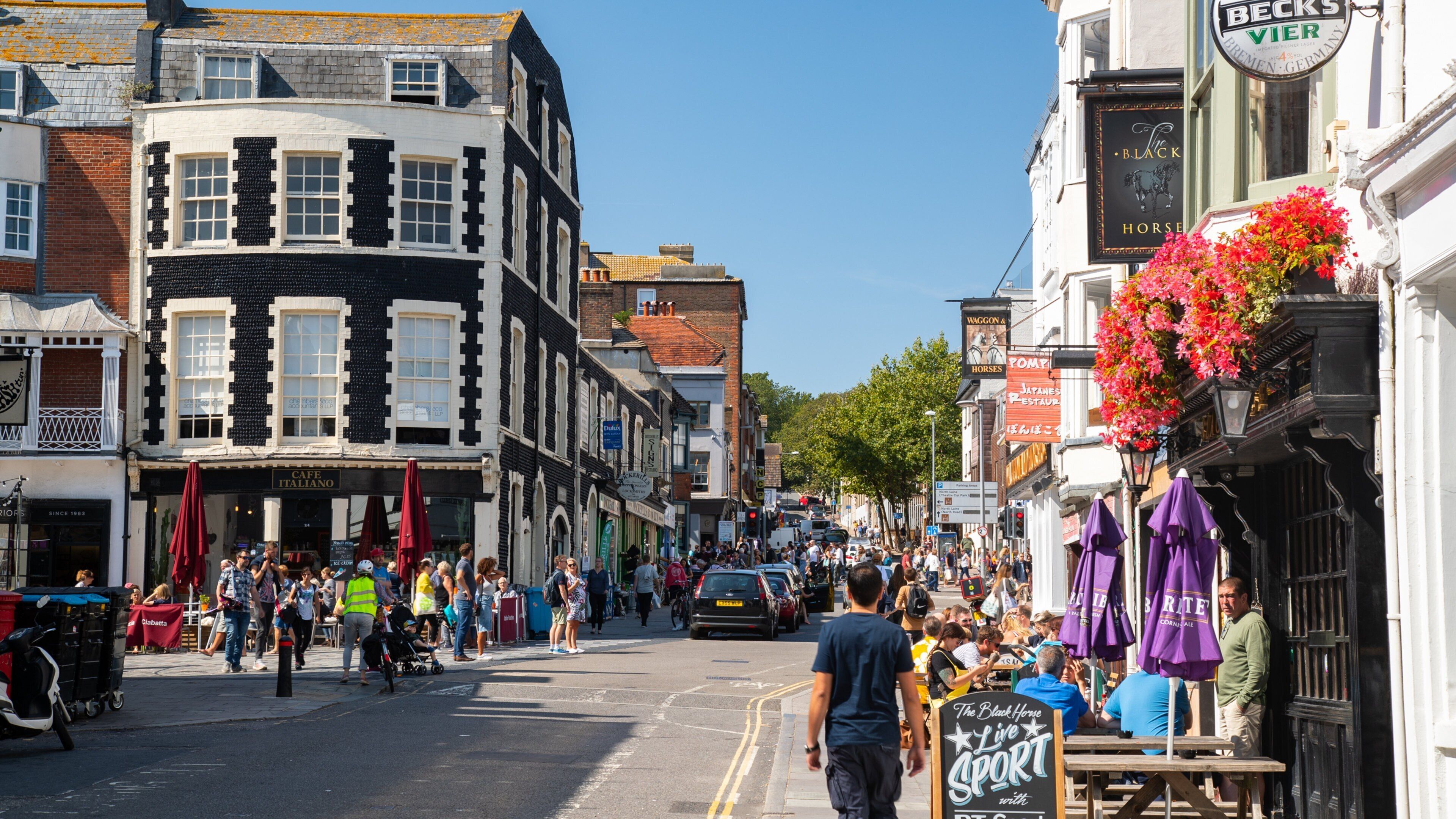 A busy street with shops, a sign for 'The Black Horse' pub, and pedestrians.