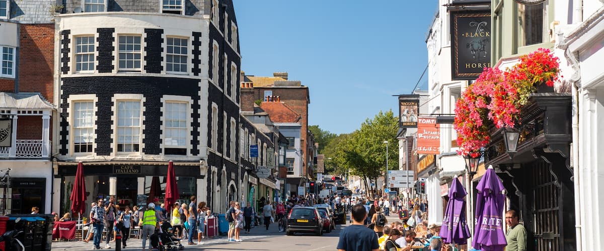 A busy street with shops, a sign for 'The Black Horse' pub, and pedestrians.