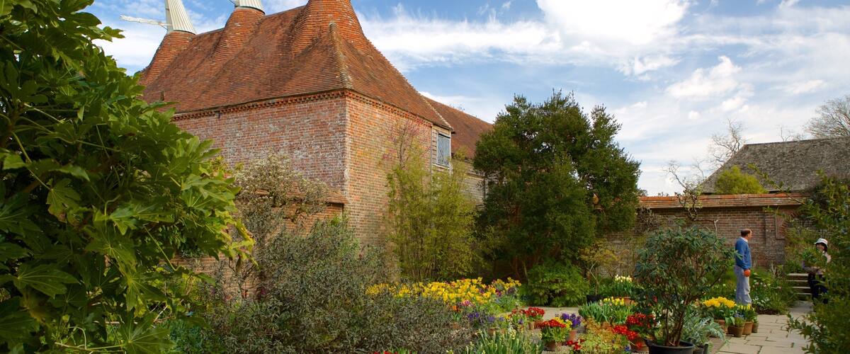 A garden with a brick building, flowering plants, and a stone bench.