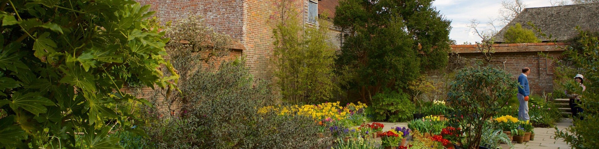 A garden with a brick building, flowering plants, and a stone bench.