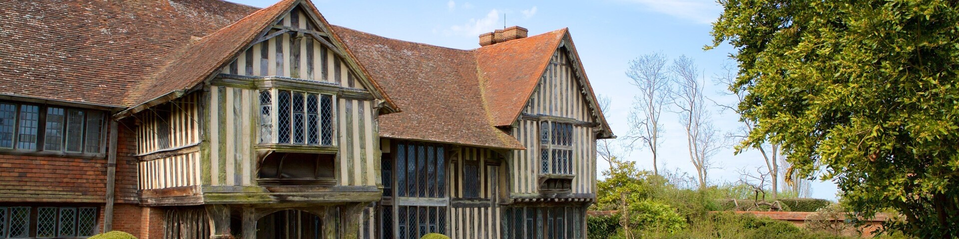 Una casa de estilo Tudor con fachada de ladrillo, estructura de madera y un jardín cuidado con setos y plantas florecientes.